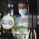 Chef in safety mask hanging up sign closed on restaurant door.