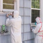 Two house painters in hazmat suits removing lead paint from an old house.