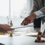 Two lawyers are discussing and reviewing a contract on a clipboard, with a gavel and scales of justice in the foreground, symbolizing legal proceedings and justice Two lawyers are discussing and reviewing a contract on a clipboard, with a gavel and scales of justice in the foreground, symbolizing legal proceedings and justice